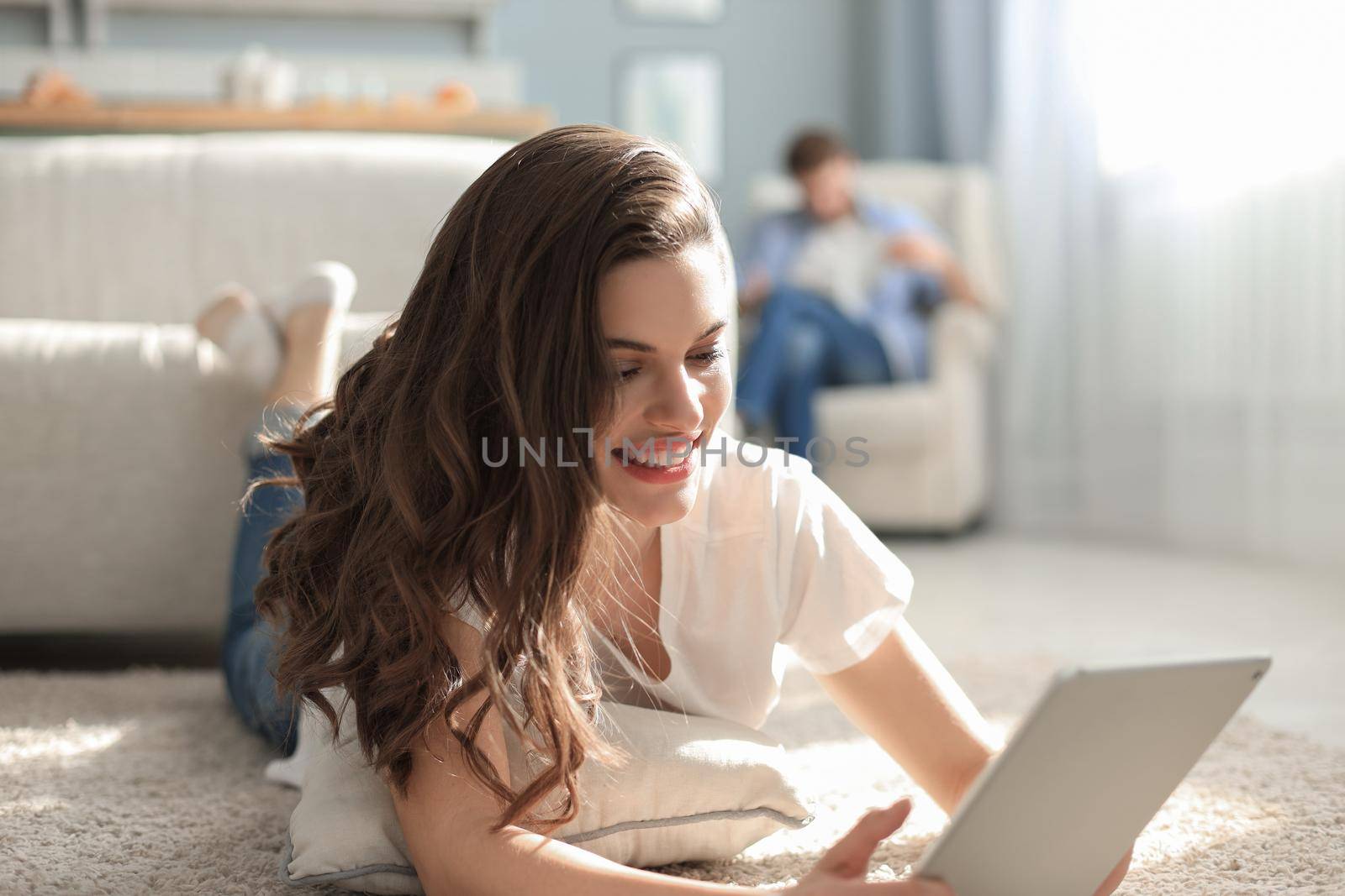 Smiling beautiful woman using tablet with blurred man in background at home
