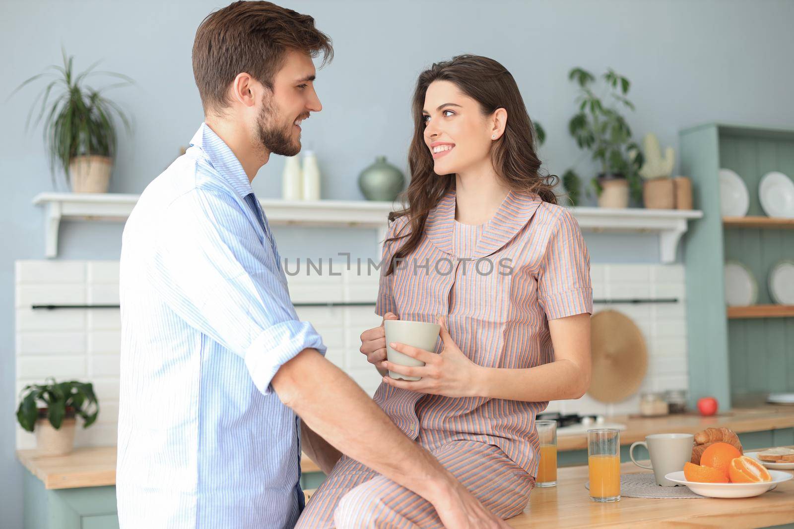 Beautiful young couple in pajamas is looking at each other and smiling while cooking in kitchen at home