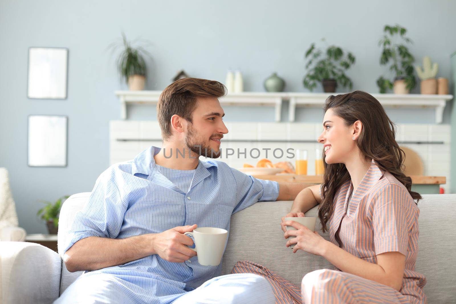Beautiful young couple in pajamas is looking at each other and smiling on a sofa in the living room