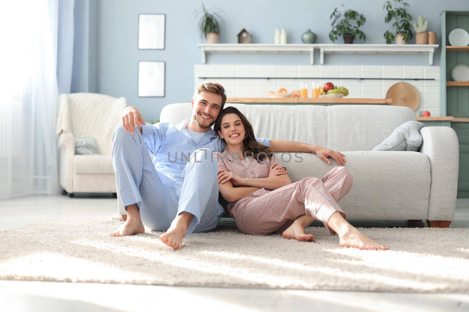 The happy couple in pajamas sitting on the floor background of the sofa in the living room