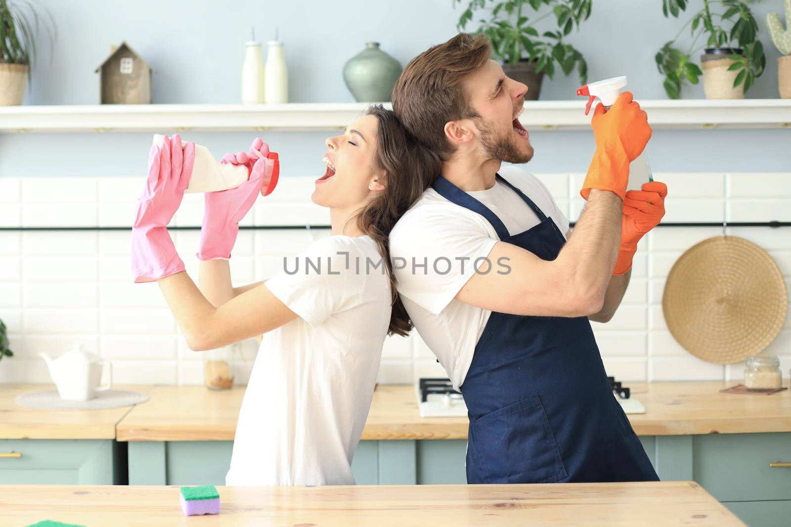 Young happy couple is having fun while doing cleaning and singing at home