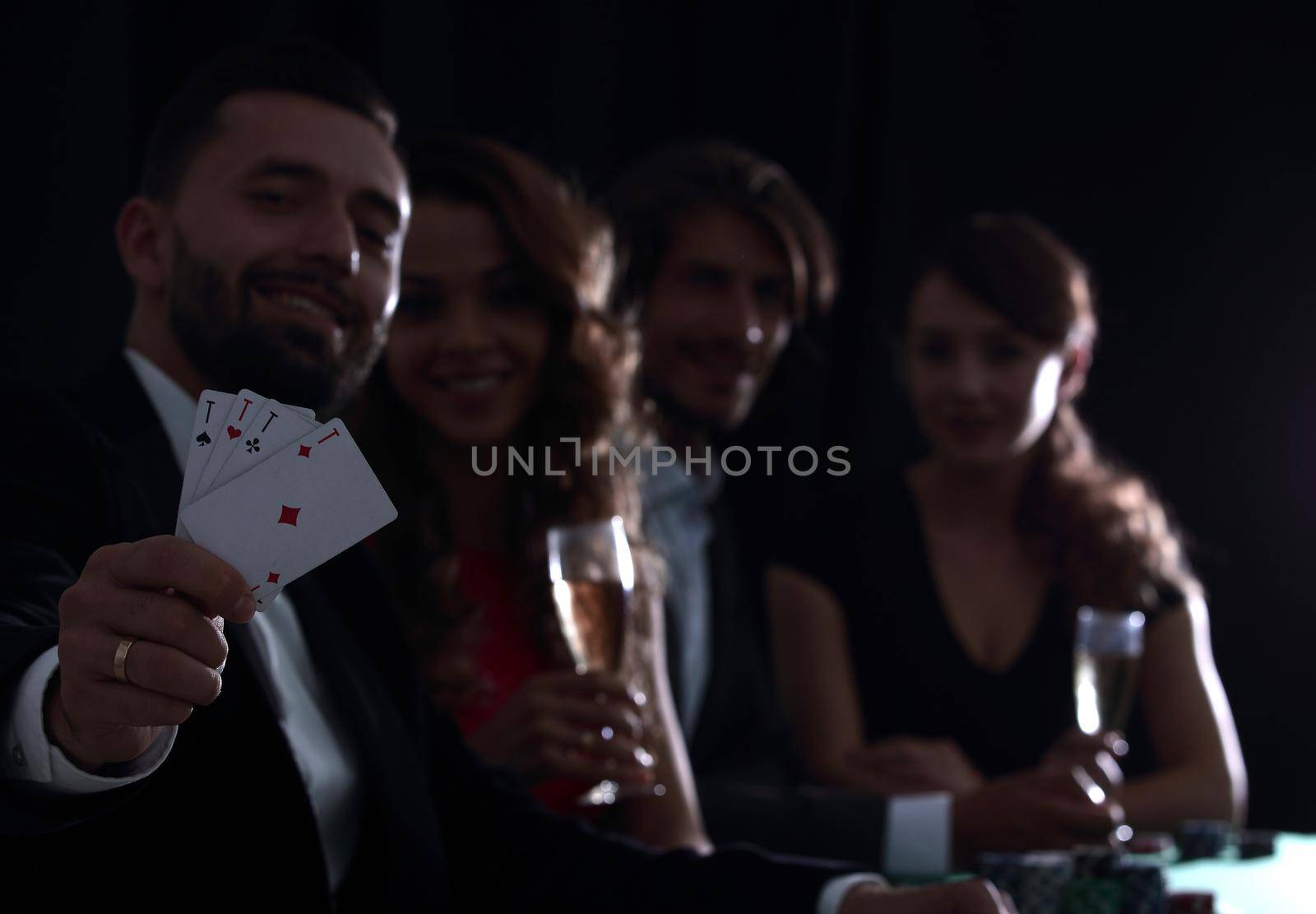 Elegant young smiling people are drinking wine at the poker table