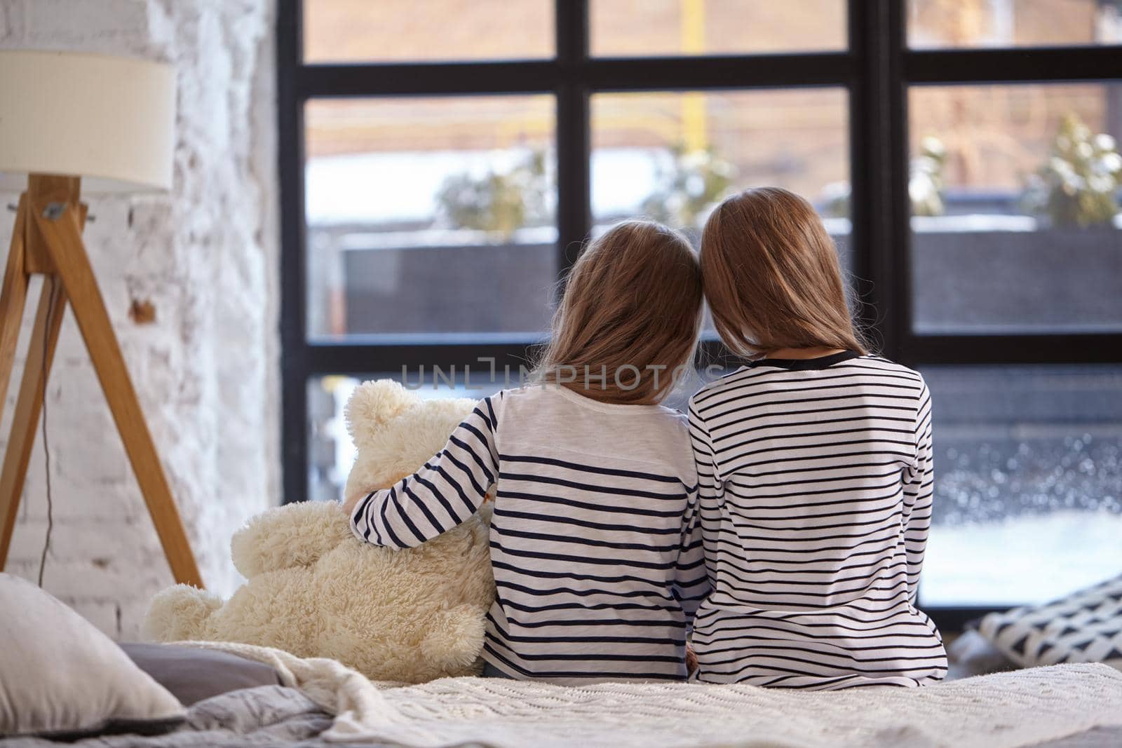 The image of two little sisters sitting on the bed in the room. by nazarovsergey