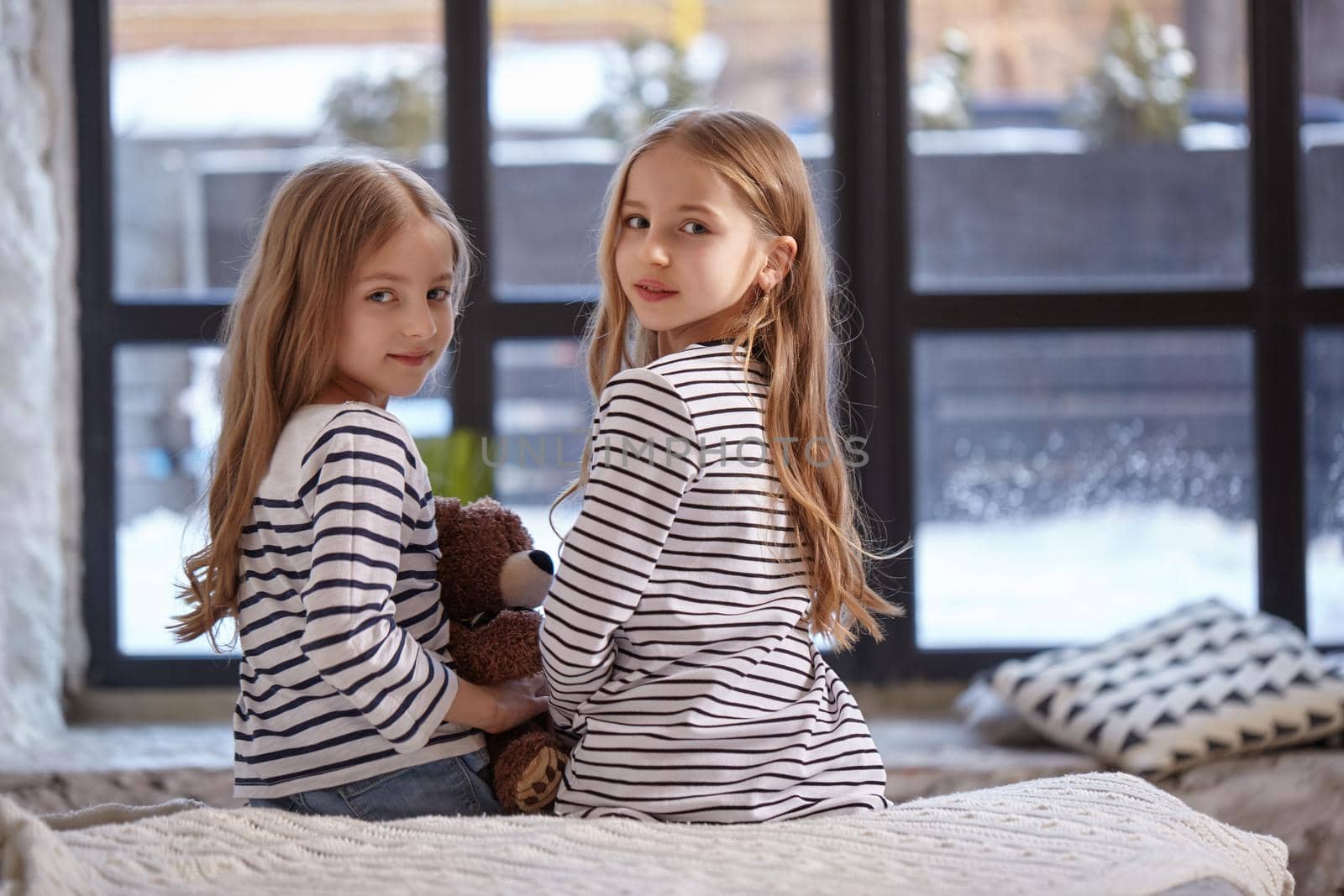 The image of two little sisters sitting on the bed in the room. by nazarovsergey