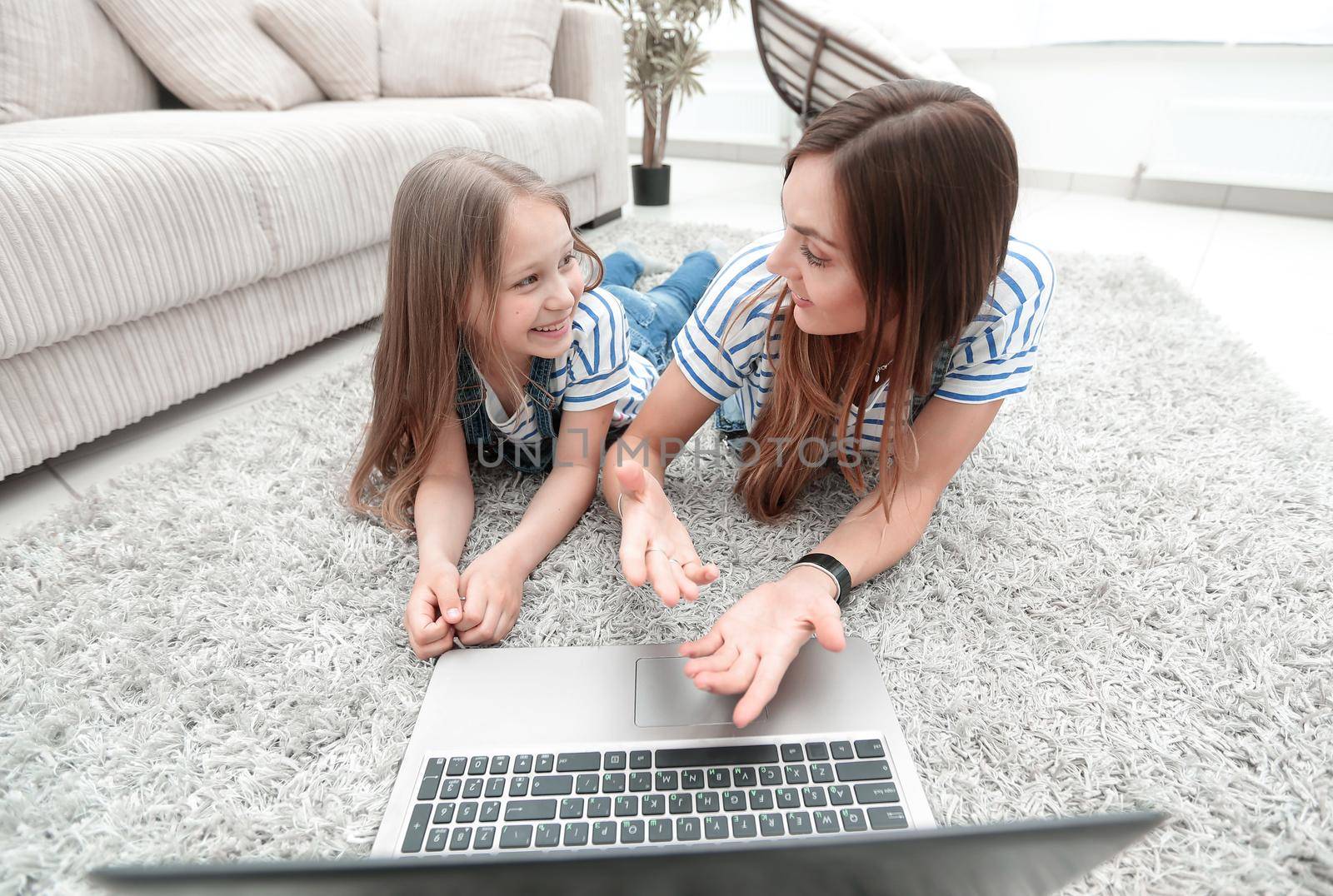 mom and daughter lying on the carpet and using a laptop by asdf