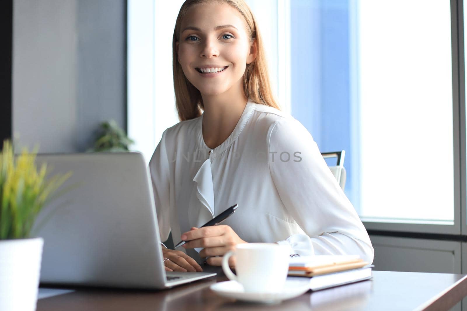 Beautiful smiling business woman is sitting in the office and looking at camera.