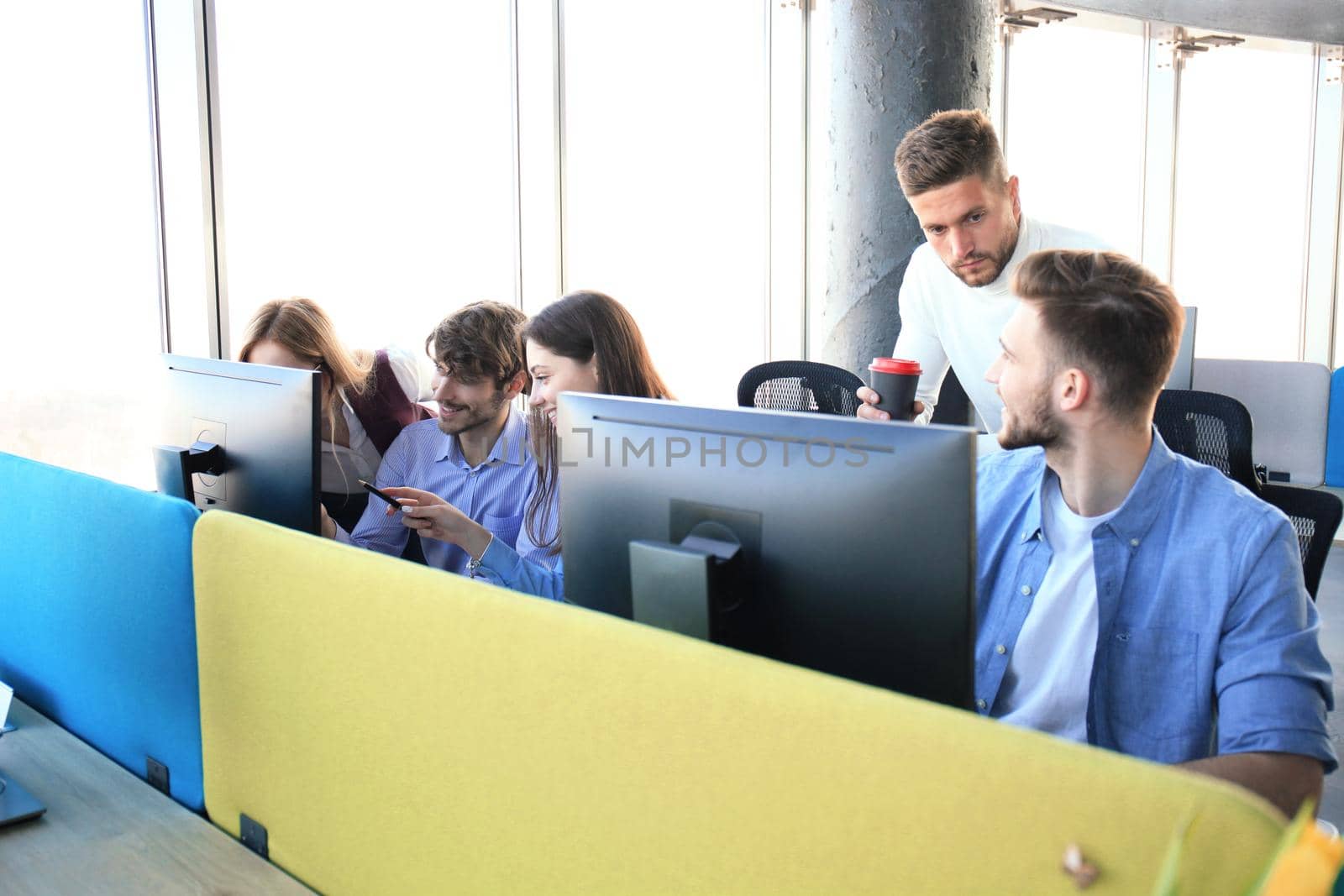 Group of young people in casual wear sitting at the office desk and discussing something while looking at PC together