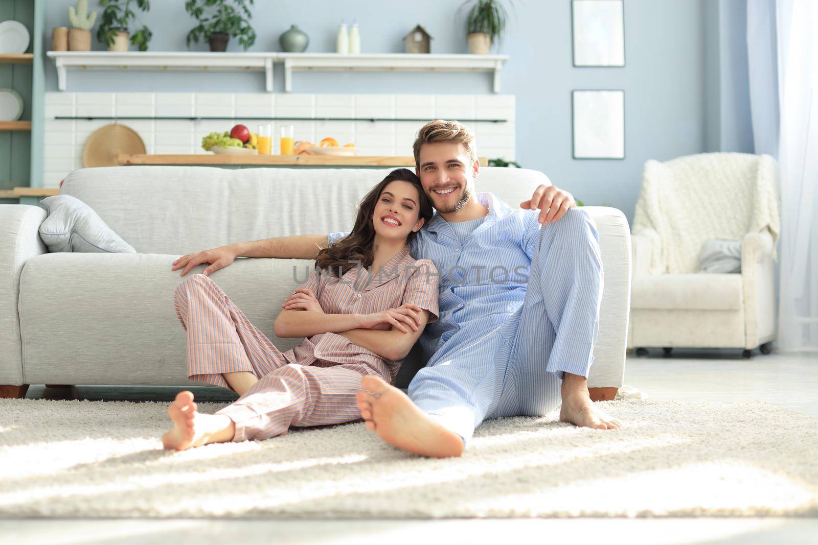 The happy couple in pajamas sitting on the floor background of the sofa in the living room