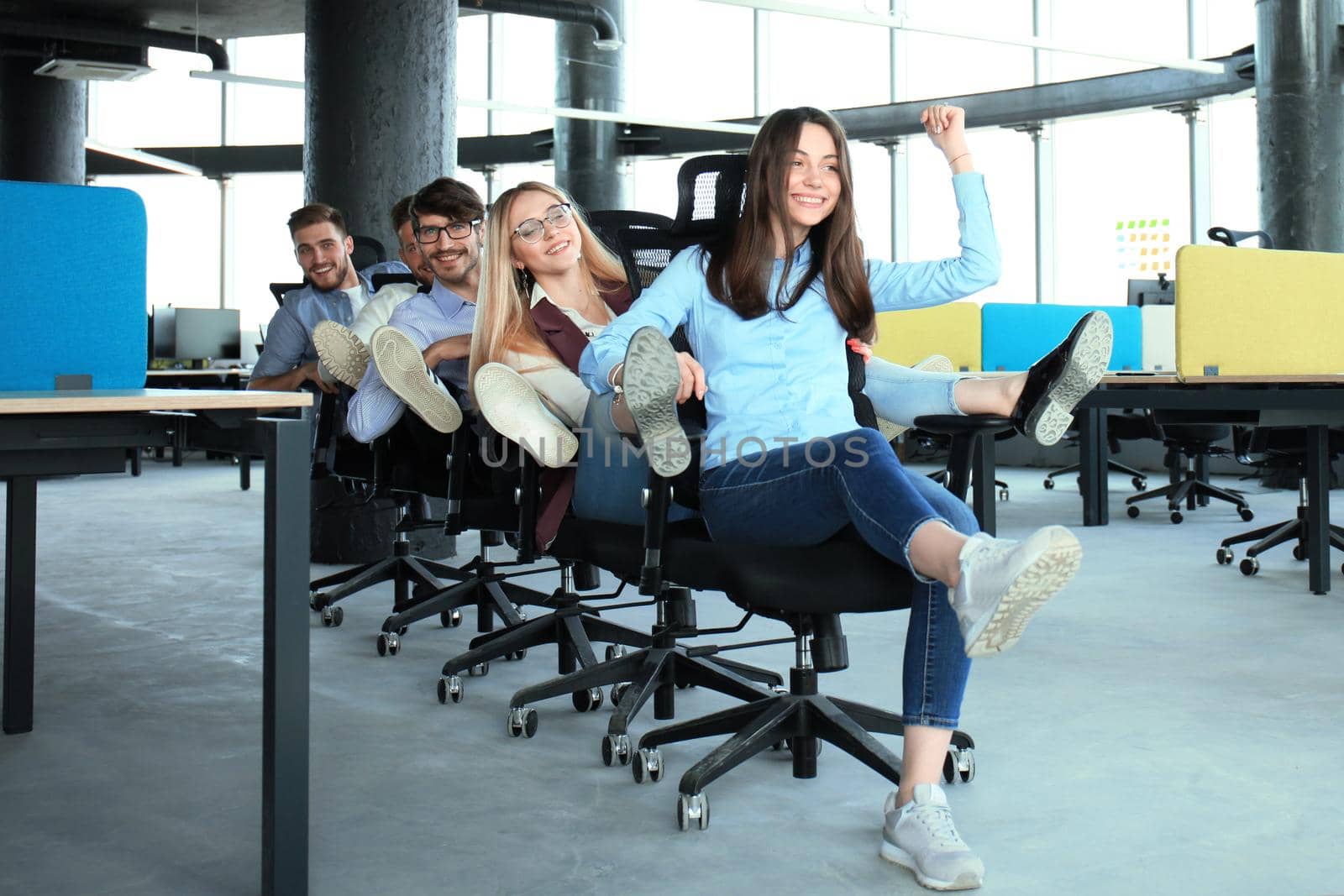 Young cheerful business people in smart casual wear having fun while racing on office chairs and smiling. by tsyhun