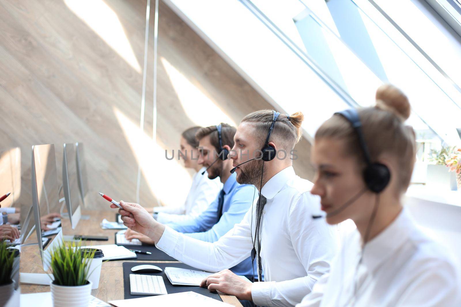 Portrait of call center worker accompanied by his team. Smiling customer support operator at work