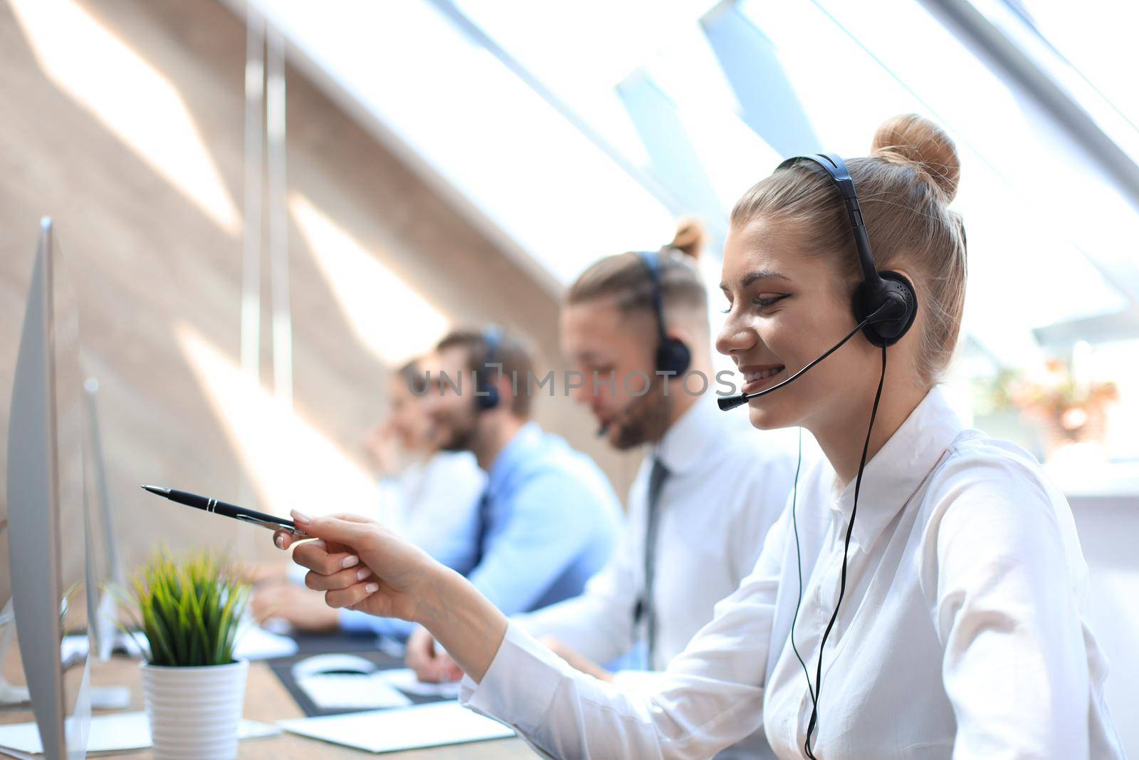 Female customer support operator with headset and smiling accompanied by her team