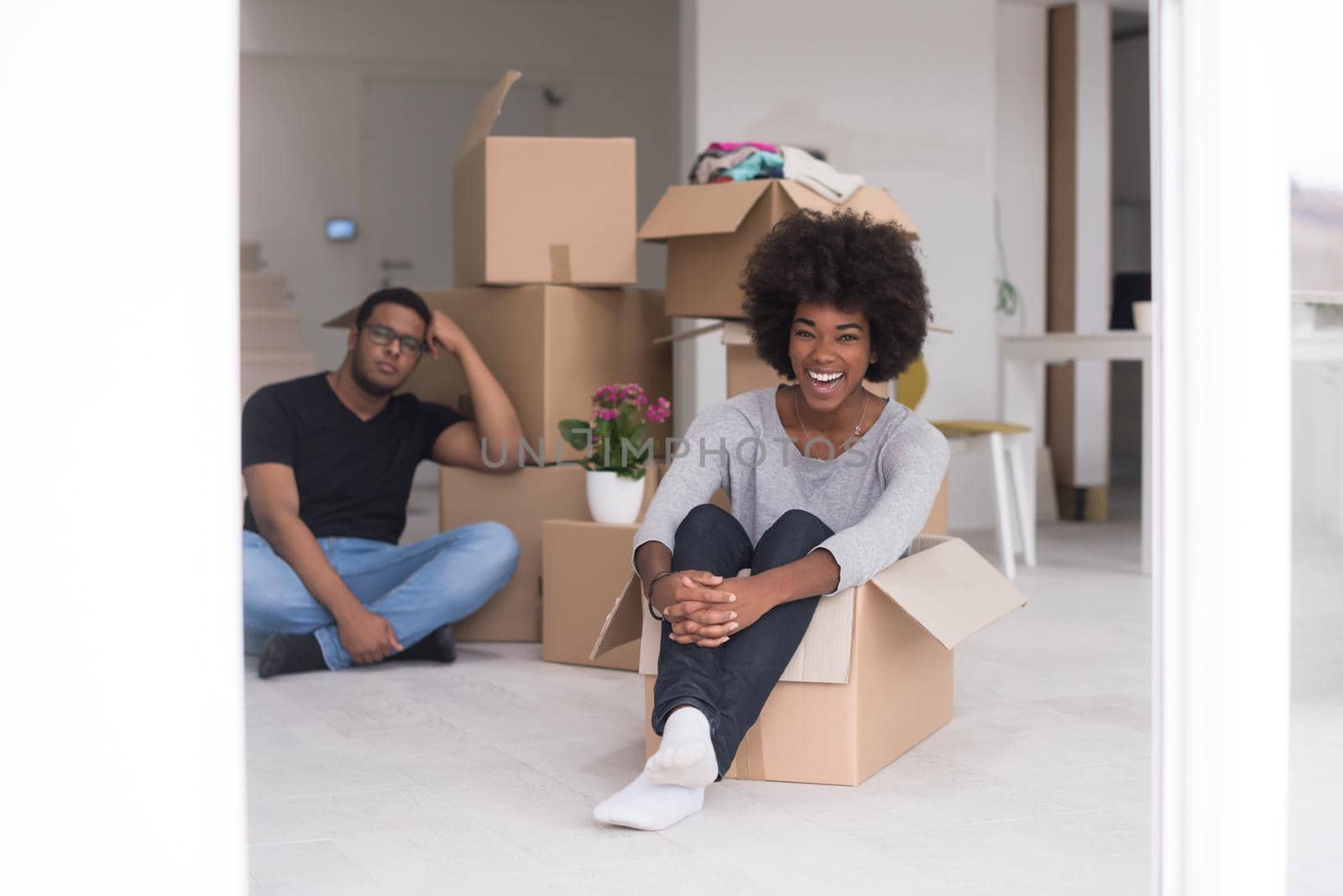 African American couple sitting in a box playing with packing material, having fun after moving in new home