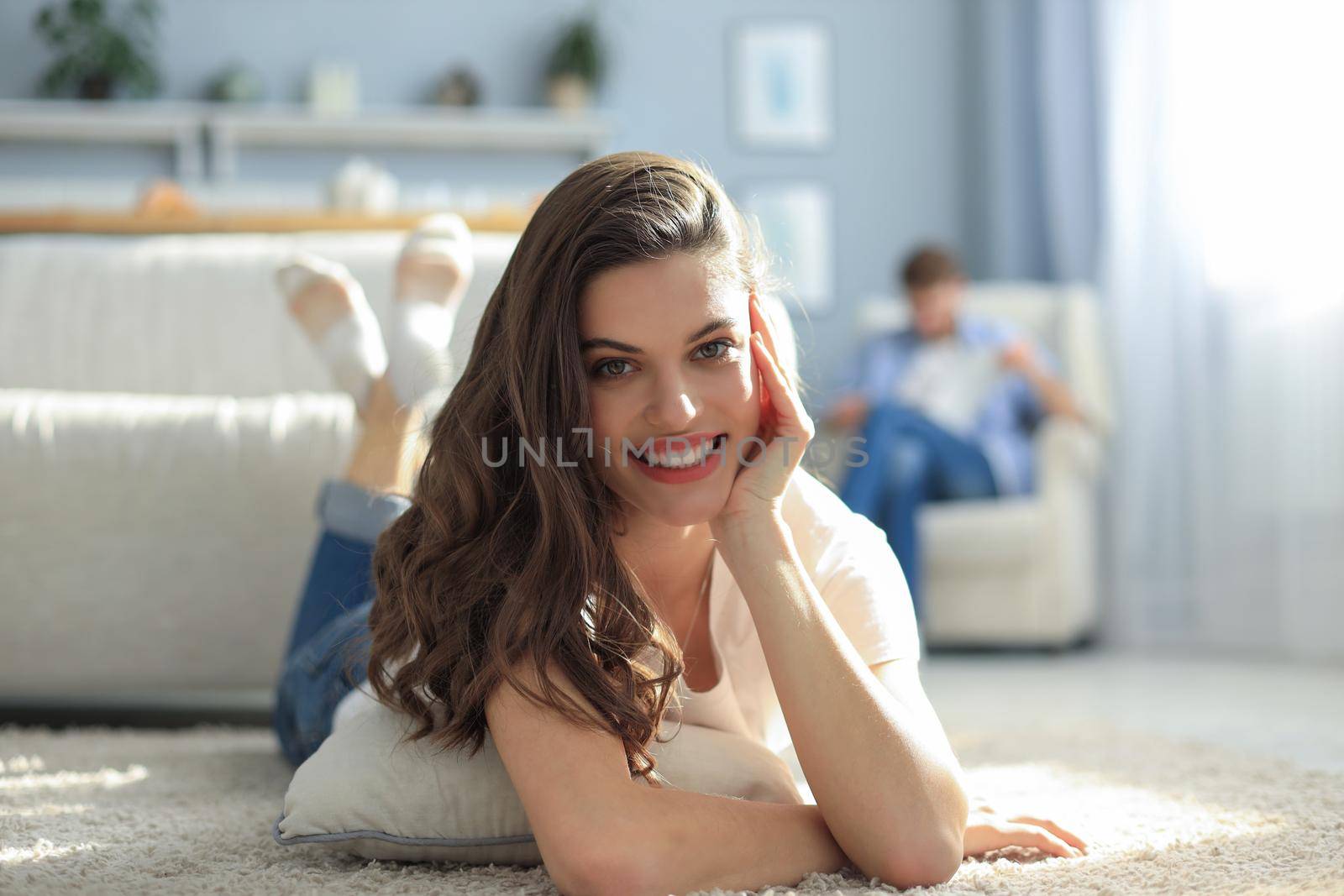 Portrait of attractive woman relaxing on floor with blurred man in background