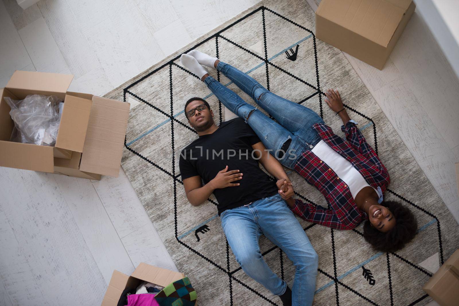 Top view of attractive young African American couple moving, holding hands, looking at camera and smiling while lying among cardboard boxes