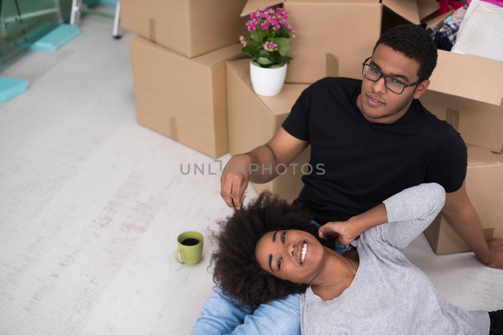 Relaxing in new house. Cheerful young African American couple sitting on the floor and drinking coffee while cardboard boxes laying all around them