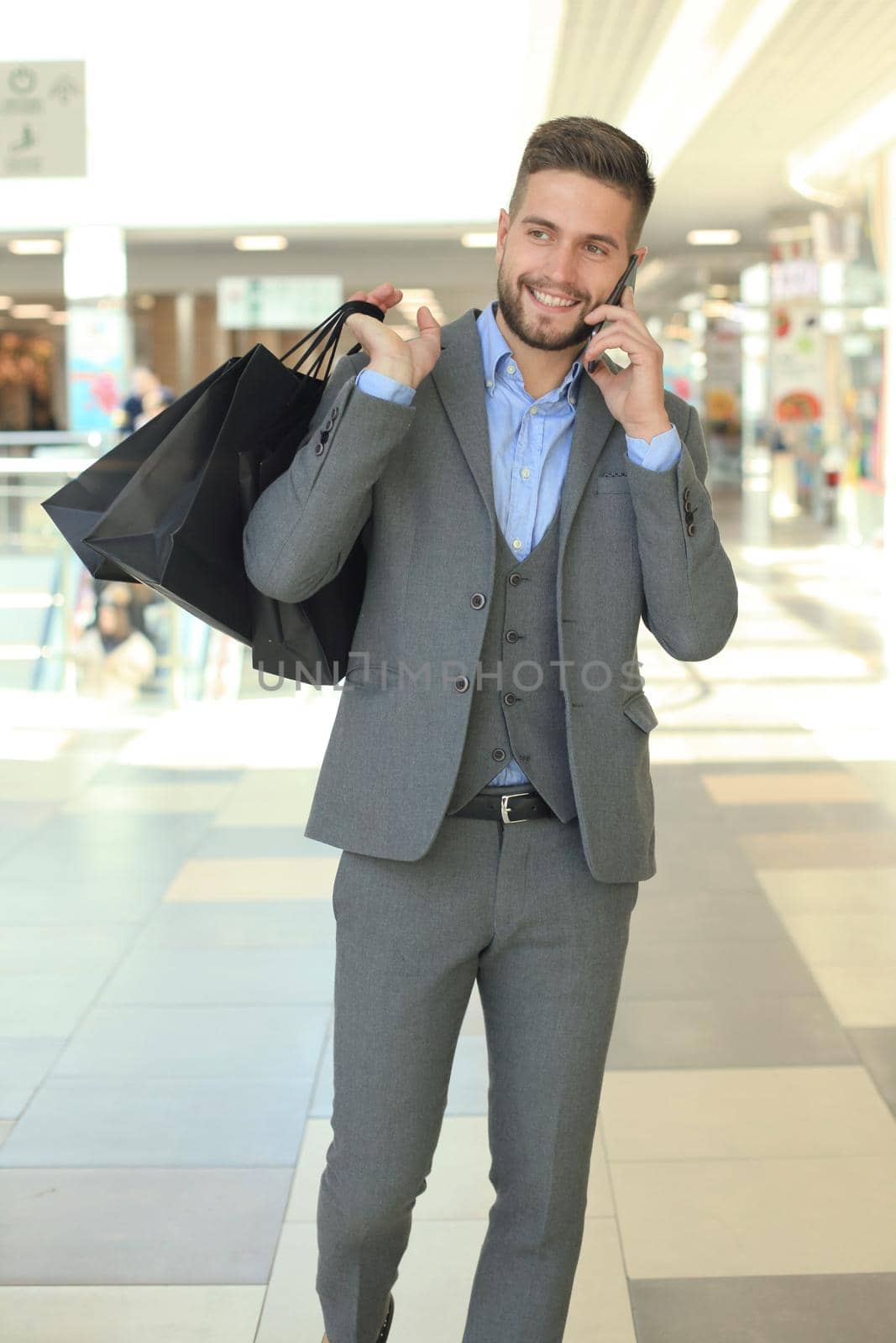 Young businessman with shopping bag talking on the phone indoors