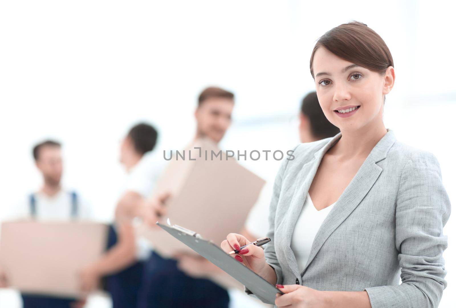 Woman manager holding clipboard on blurred background with movers and boxes.