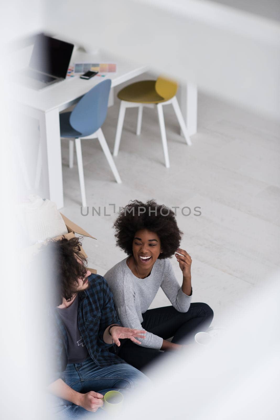 Relaxing in new house. Cheerful young multiethnic couple sitting on the floor and drinking coffee while cardboard boxes laying all around them