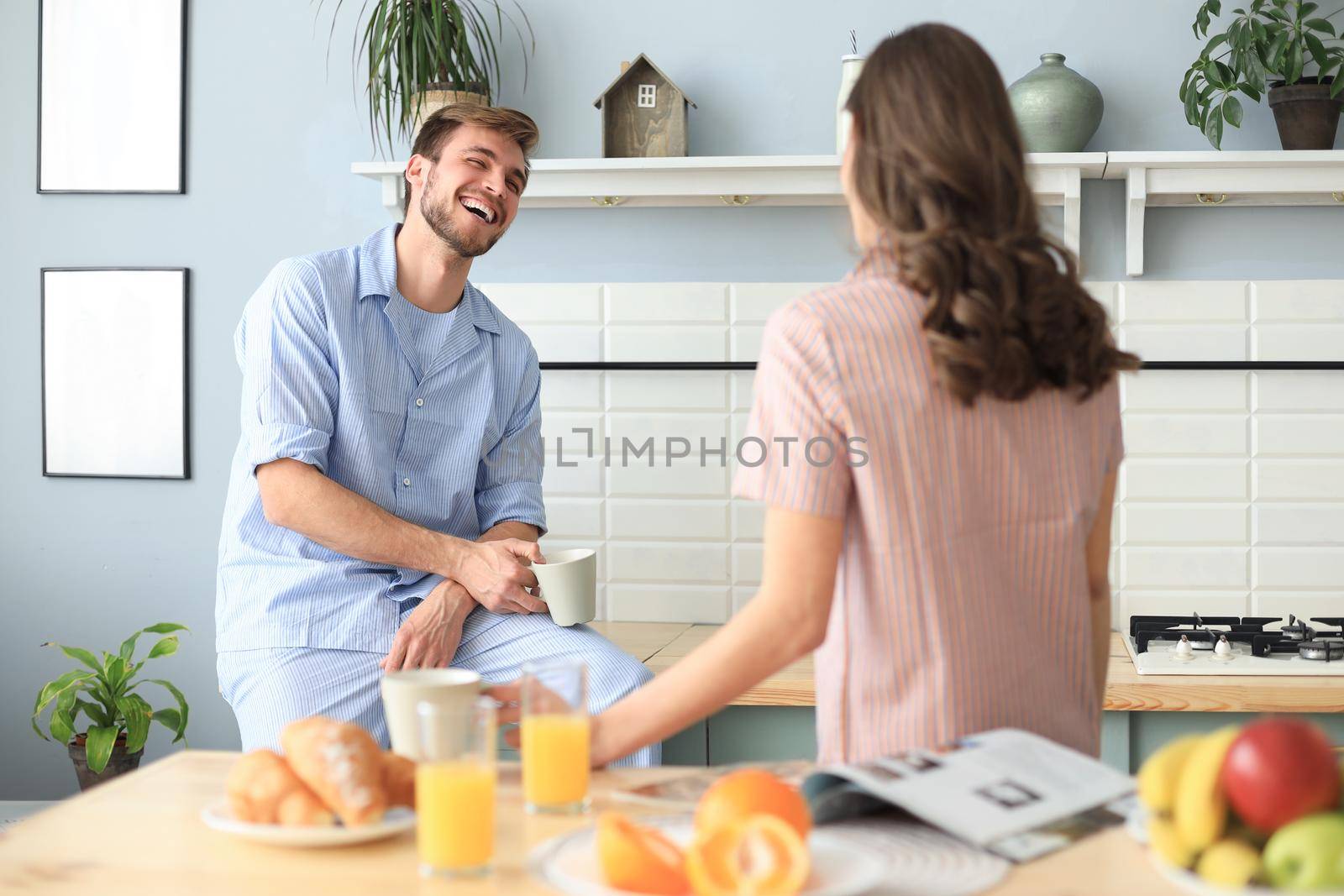 Beautiful young couple in pajamas is looking at each other and smiling while cooking in kitchen at home. by tsyhun