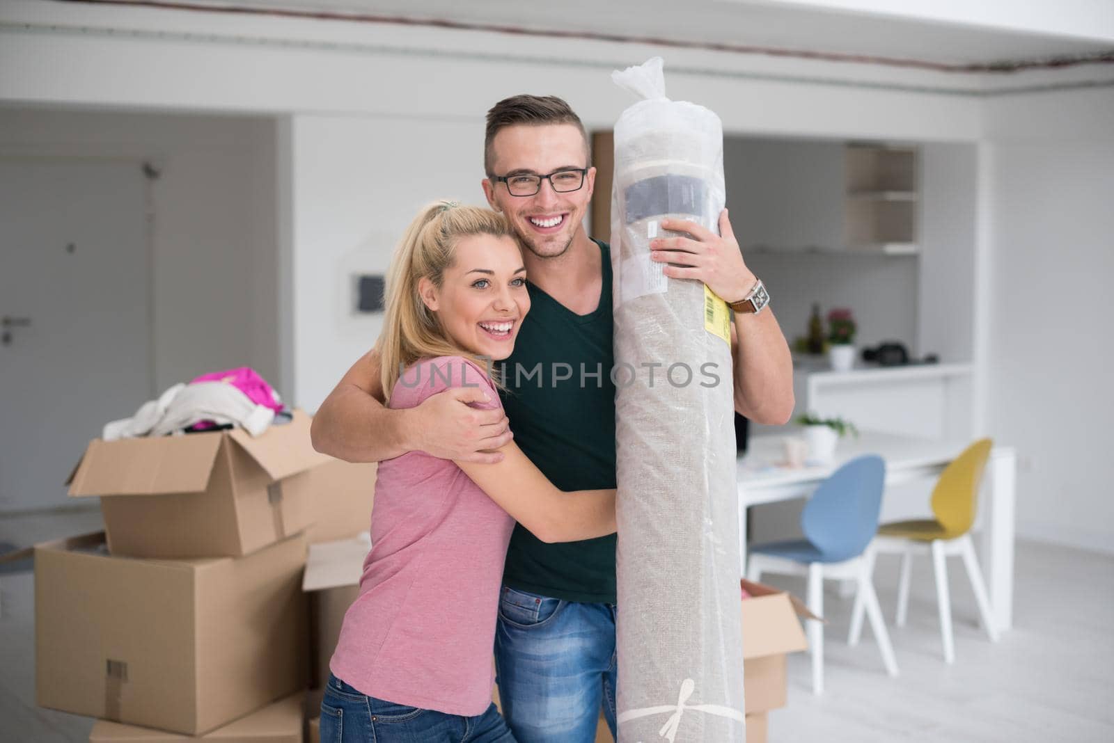 Young couple carrying a carpet moving in to new home together. Home, people, moving and real estate concept