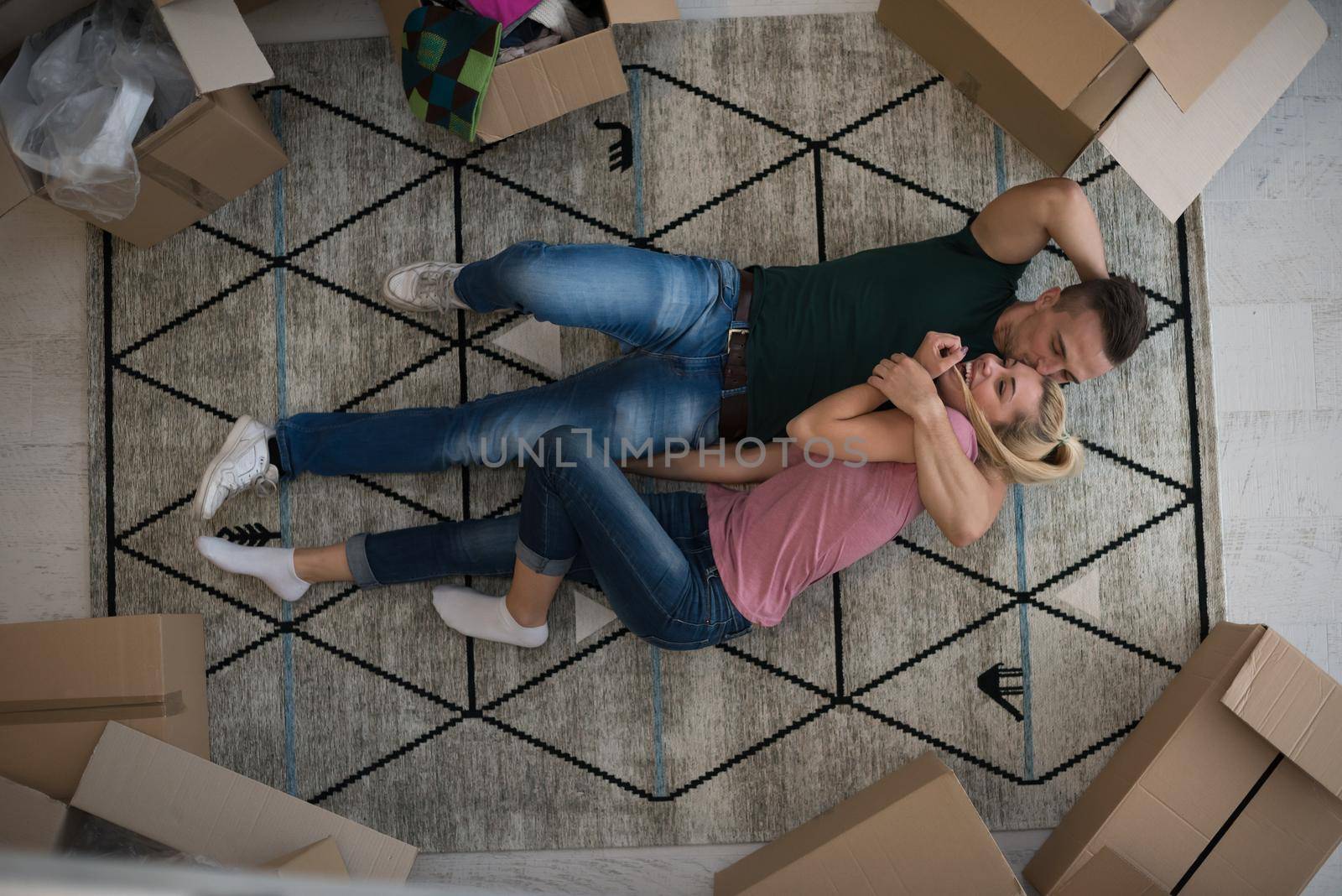 Top view of attractive young couple moving, holding hands, looking at camera and smiling while lying among cardboard boxes