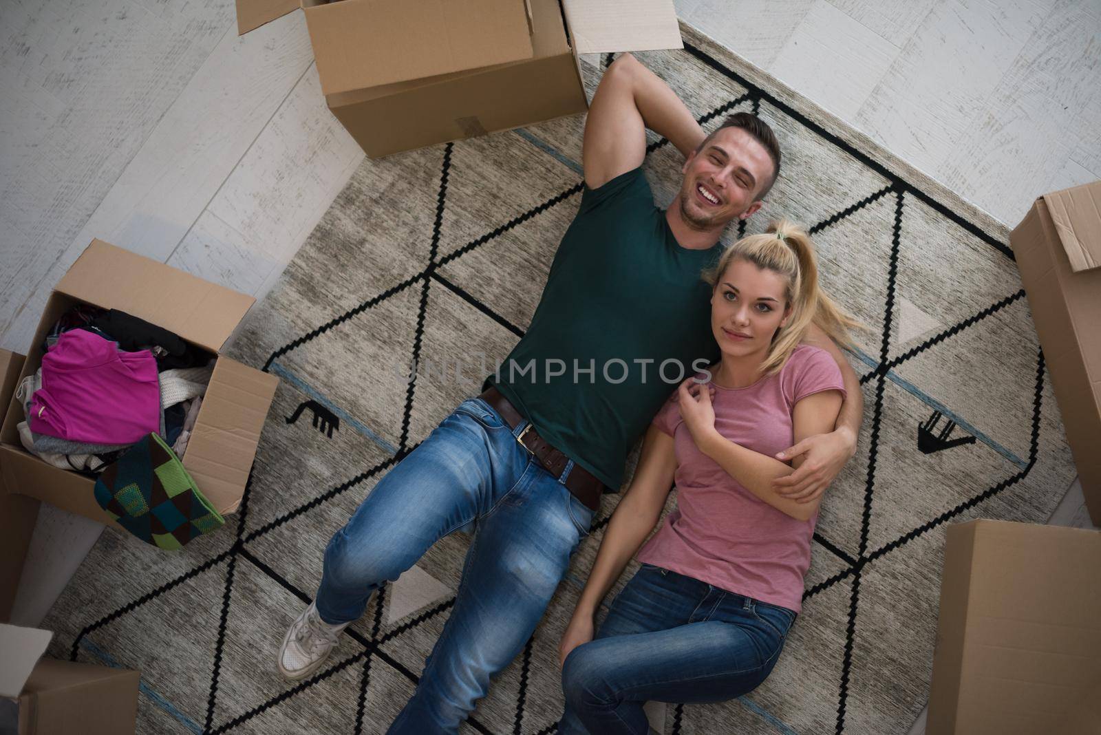 Top view of attractive young couple moving, holding hands, looking at camera and smiling while lying among cardboard boxes