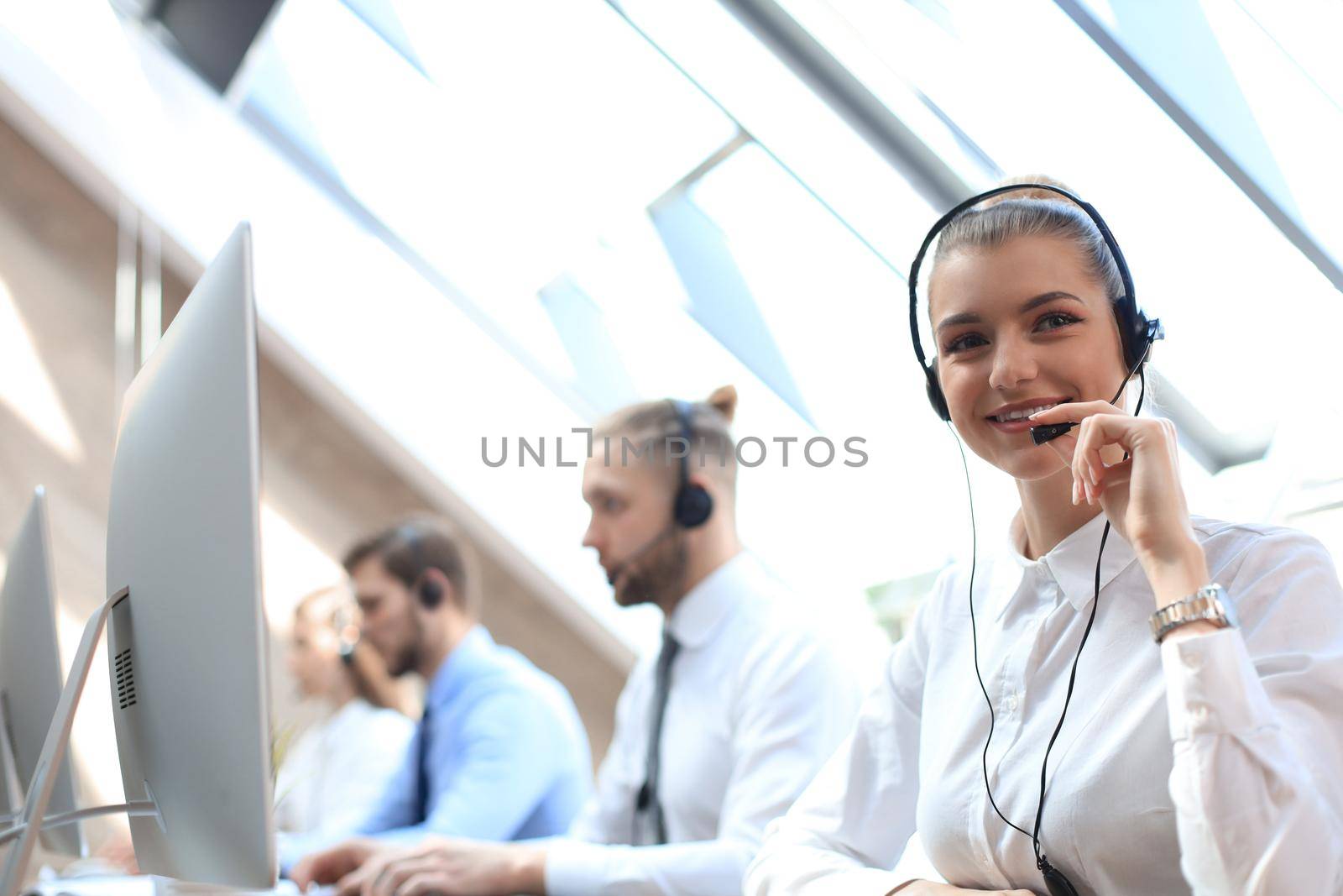 Female customer support operator with headset and smiling accompanied by her team. by tsyhun