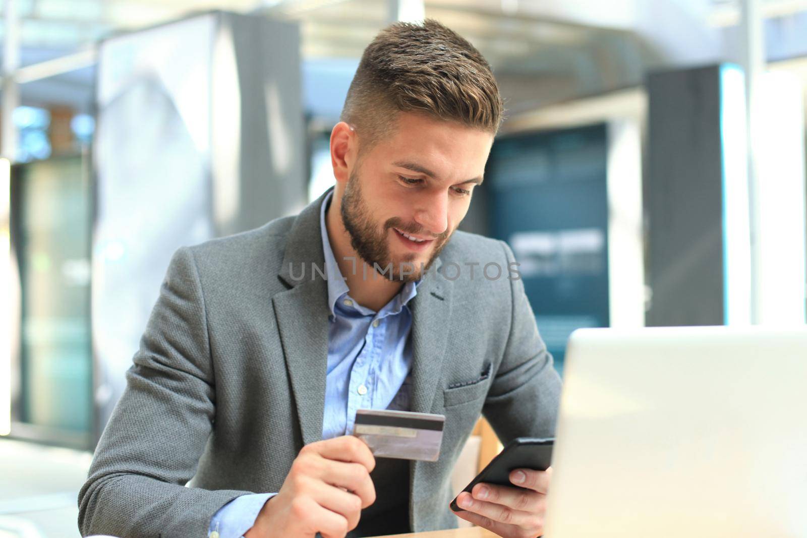 Happy young businessman using laptop and credit card at the table