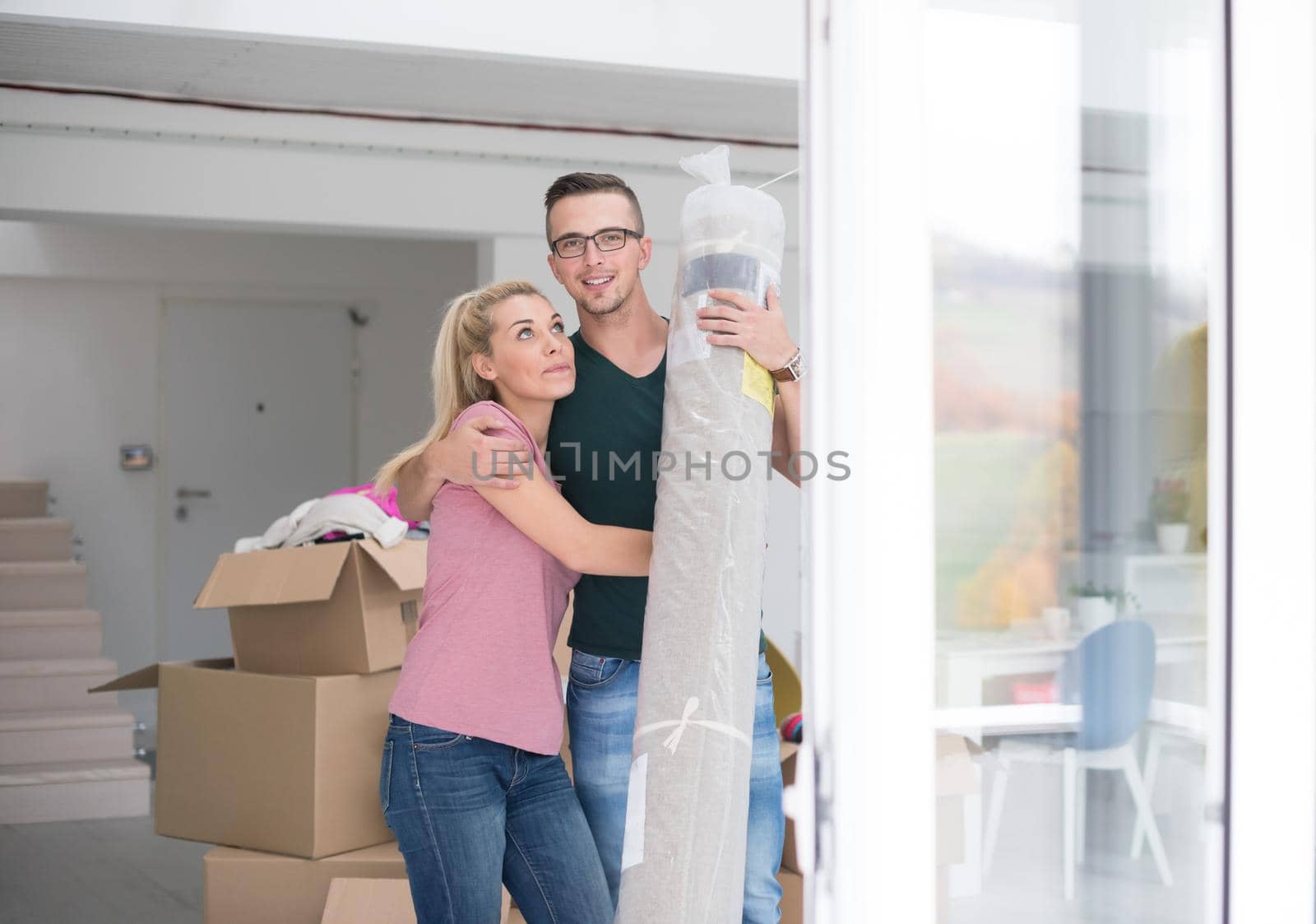 Young couple carrying a carpet moving in to new home together. Home, people, moving and real estate concept