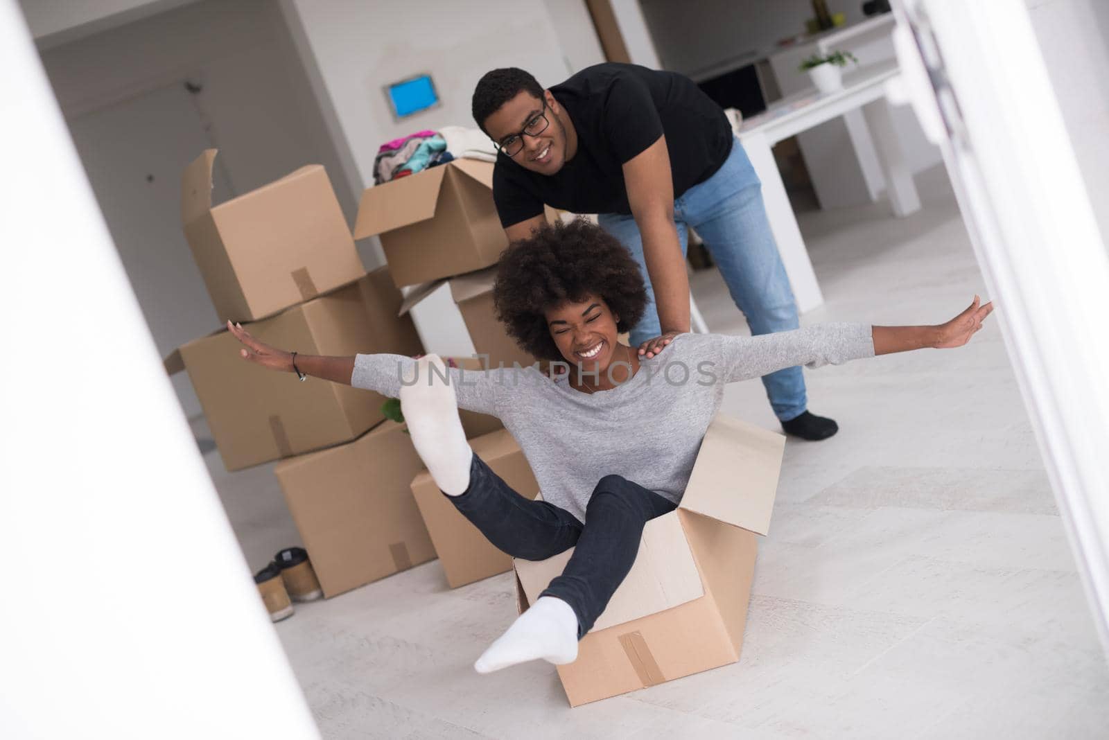 African American couple sitting in a box playing with packing material, having fun after moving in new home