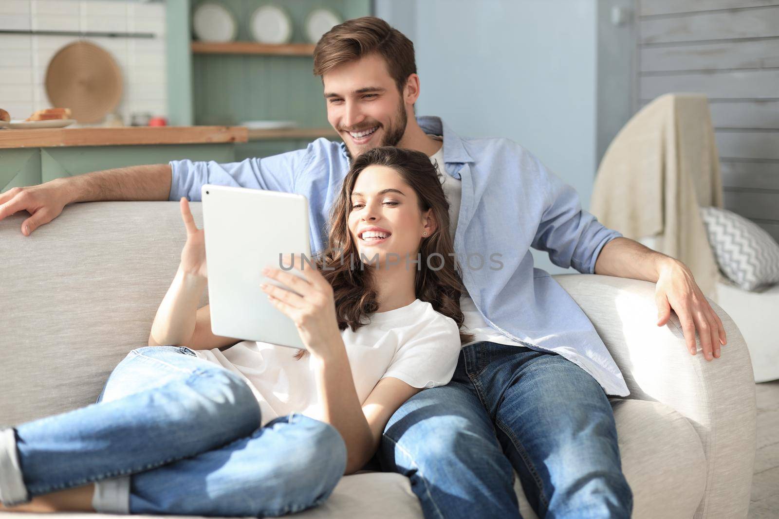 Young couple watching media content online in a tablet sitting on a sofa in the living room. by tsyhun