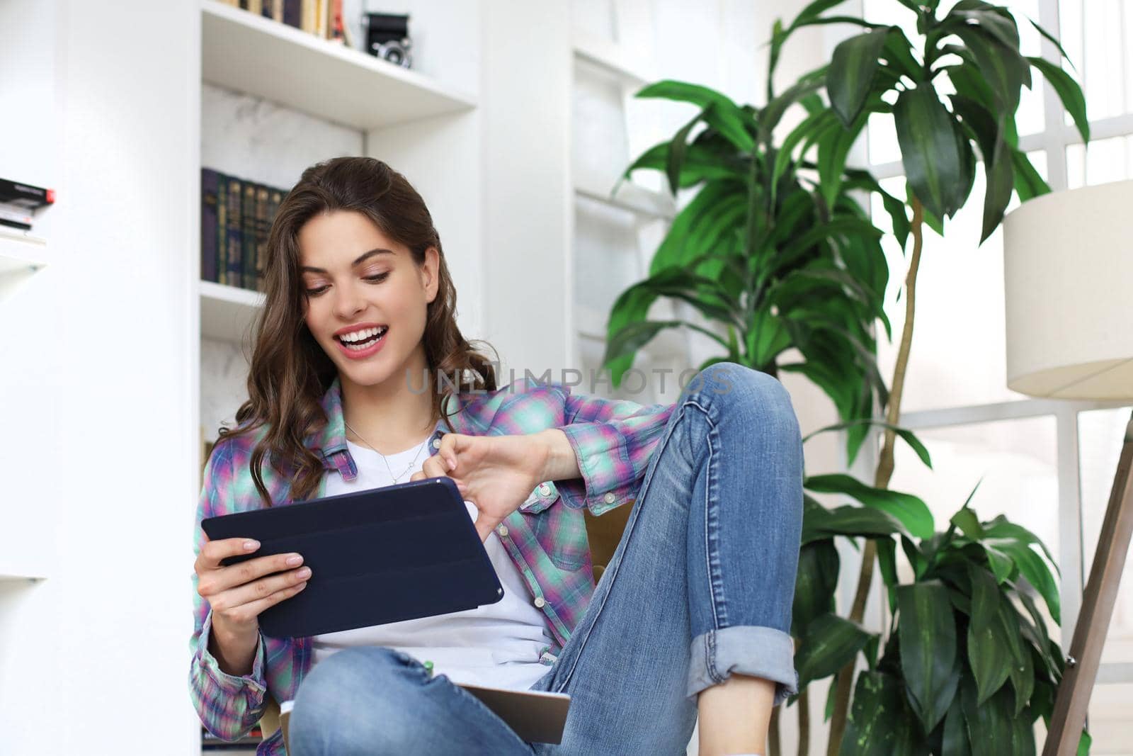 Smiling young female sitting on the floor in the living room, student studying at home working with her tablet. Distance learning.