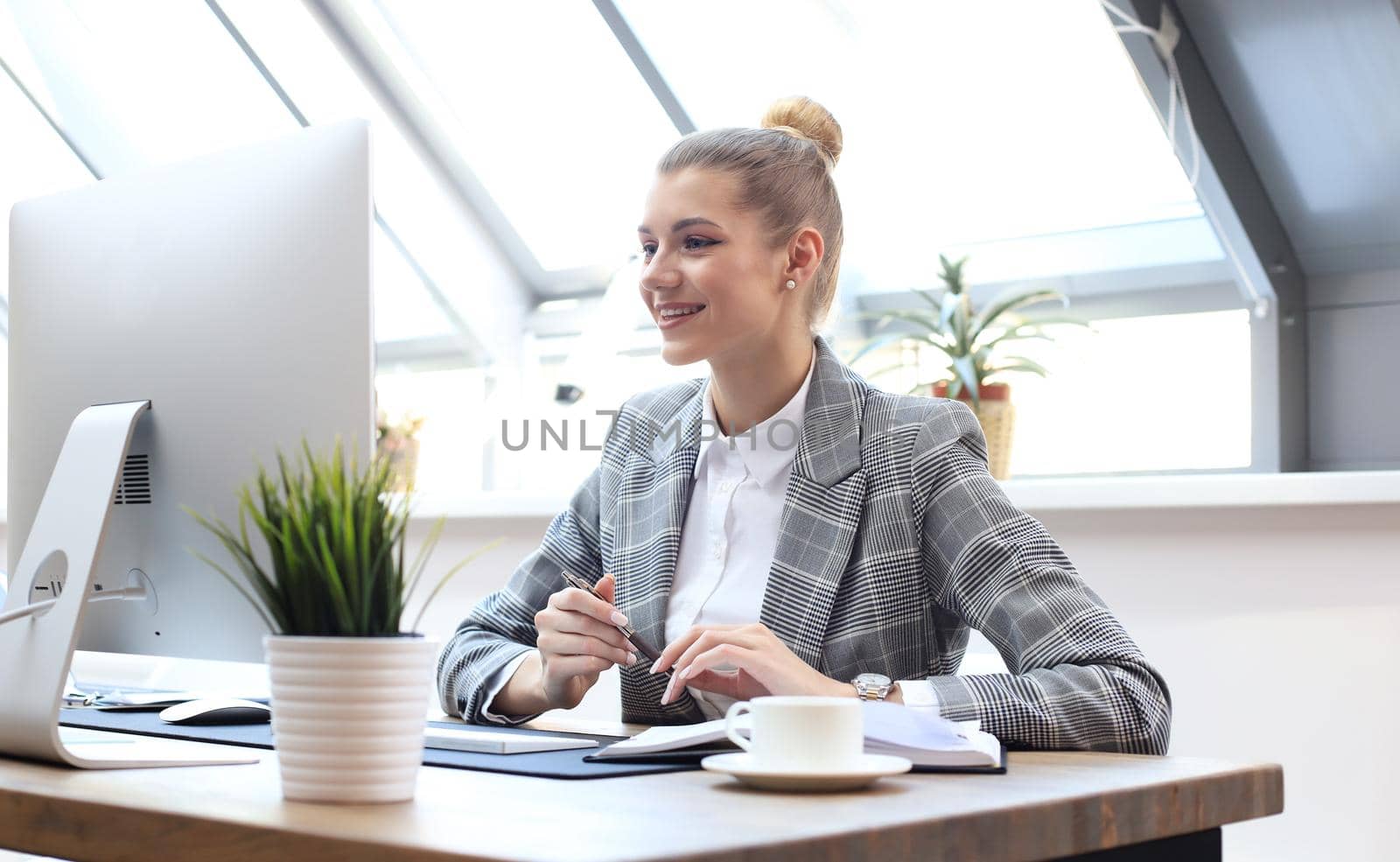 Portrait of a cheerful young businesswoman sitting at the table in office and looking at camera