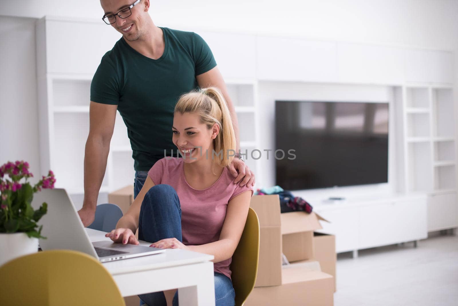 Young couple moving in a new home. Man and woman at the table using notebook laptop computer and plans with boxes around them