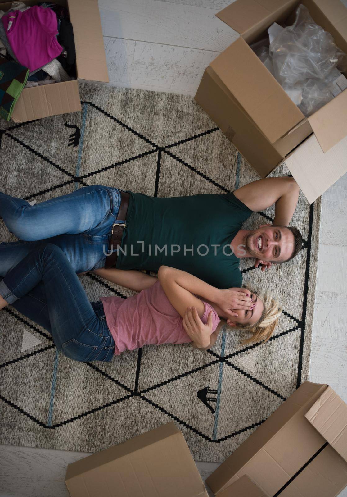 Top view of attractive young couple moving, holding hands, looking at camera and smiling while lying among cardboard boxes