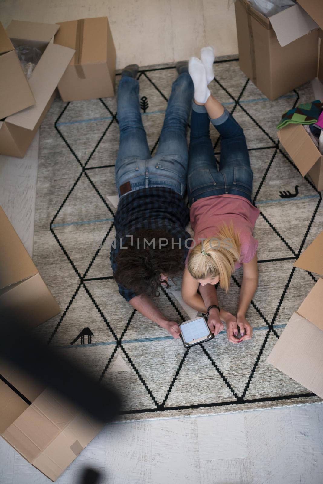 Top view of attractive young couple moving, holding hands, looking at camera and smiling while lying among cardboard boxes