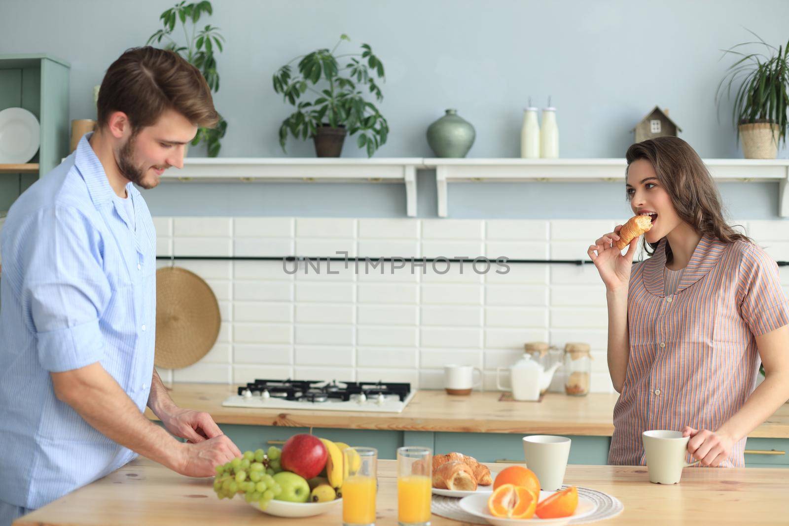 Beautiful young couple in pajamas is looking at each other and smiling while cooking in kitchen at home. by tsyhun