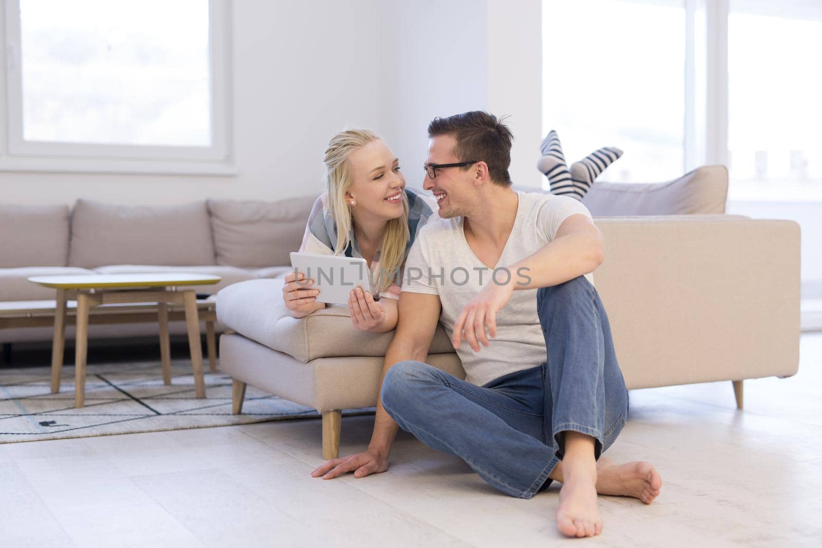 Young couple relaxing at  home using tablet computers reading in the living room on the sofa couch.