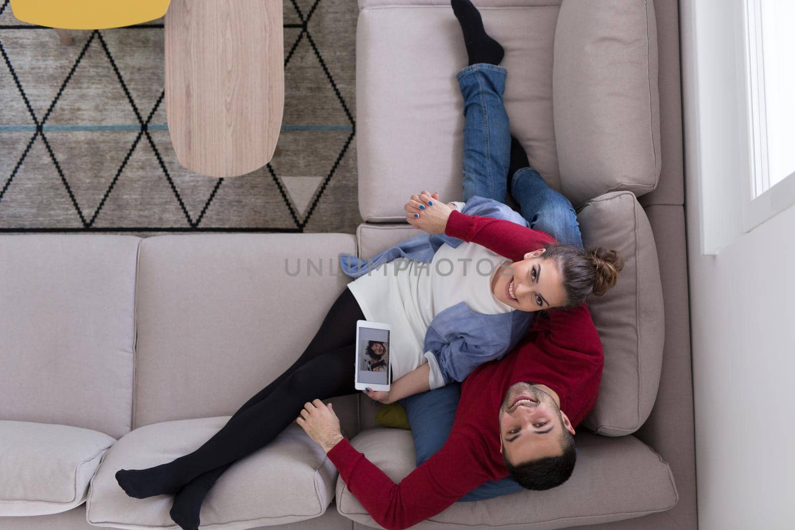 Young couple relaxing at  home using tablet computers reading in the living room on the sofa couch.