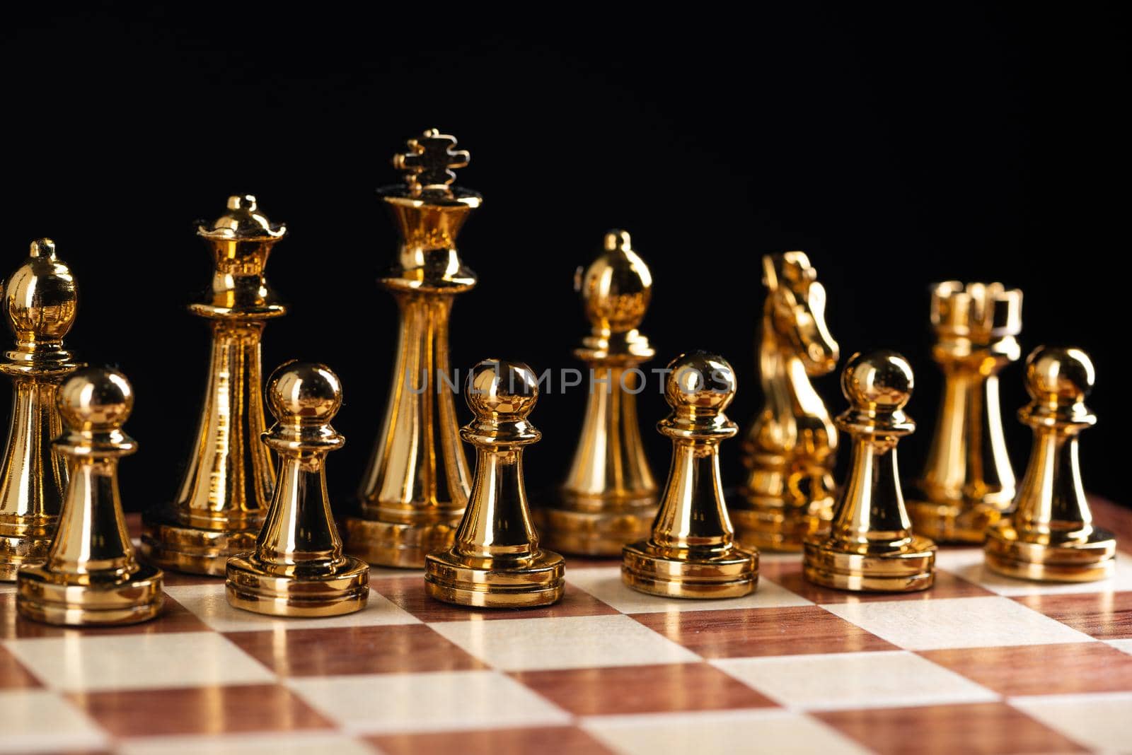 Golden chess figures standing on chessboard. Intellectual and tactic game. Strategy planning, leadership and teamwork business concept. Close-up gold chess pieces in row on black background.