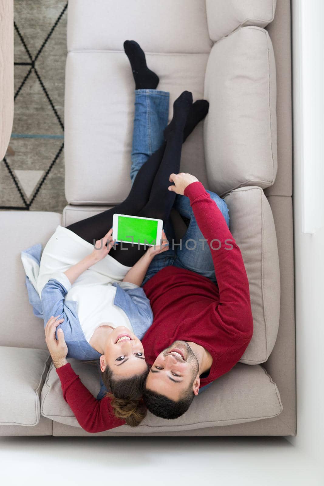 Young couple relaxing at  home using tablet computers reading in the living room on the sofa couch.