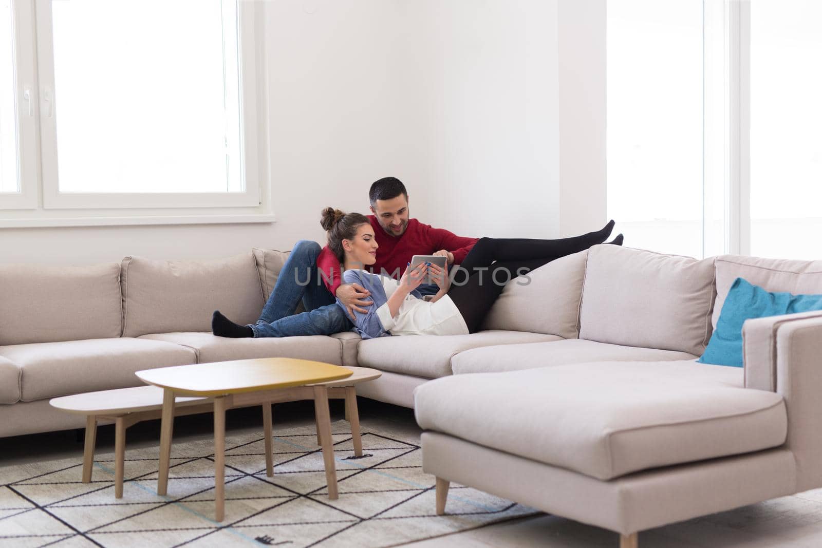 Young couple relaxing at  home using tablet computers reading in the living room on the sofa couch.