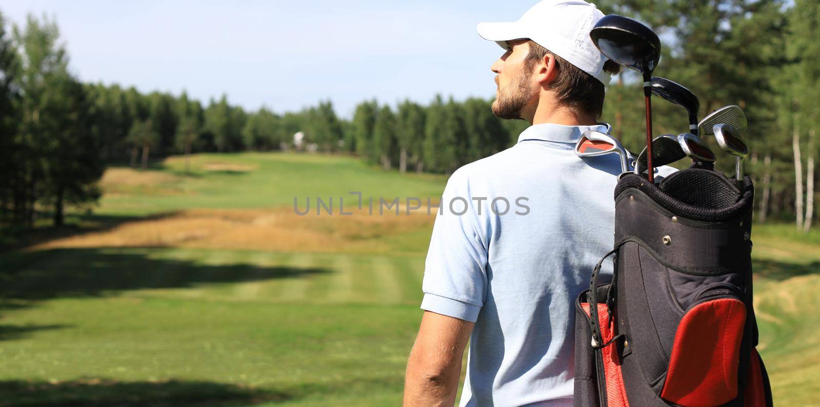 Golf player walking and carrying bag on course during summer game golfing