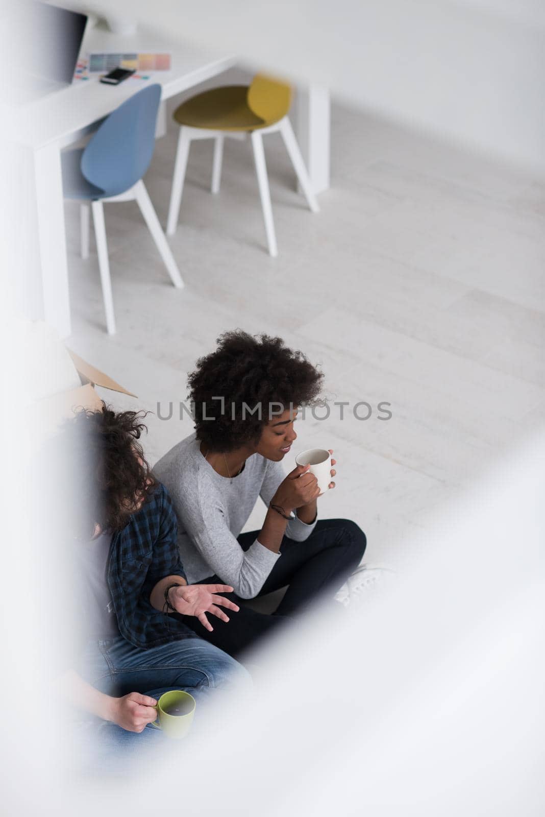 Relaxing in new house. Cheerful young multiethnic couple sitting on the floor and drinking coffee while cardboard boxes laying all around them