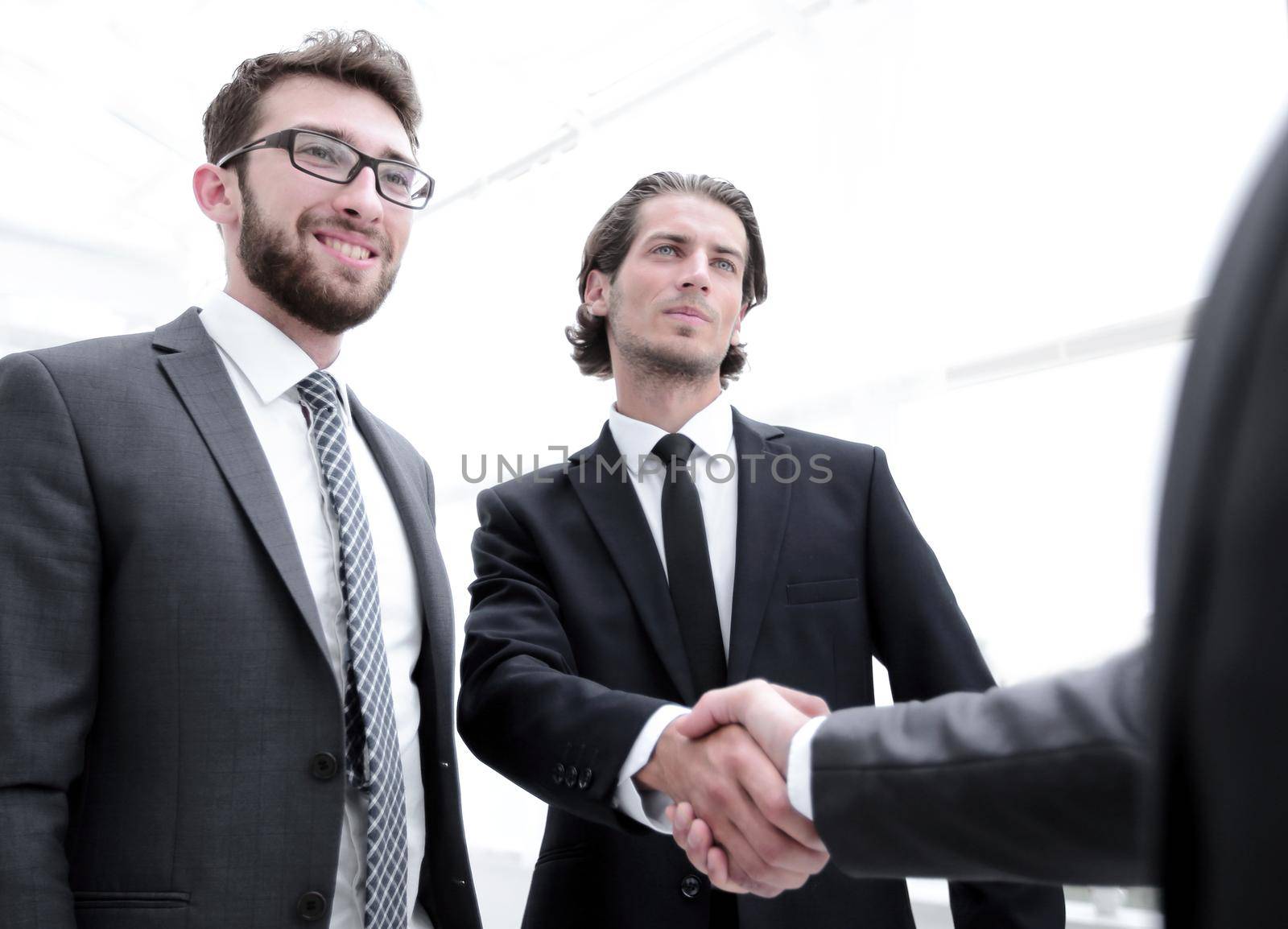 confident businessmen shaking hands and smiling while standing at office together