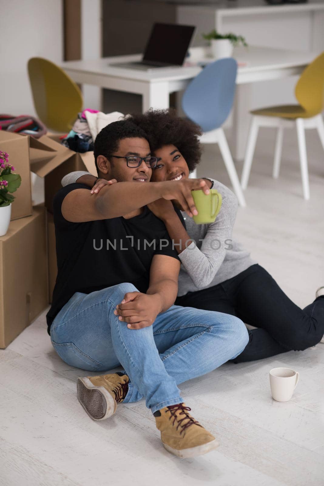 Relaxing in new house. Cheerful young African American couple sitting on the floor and drinking coffee while cardboard boxes laying all around them