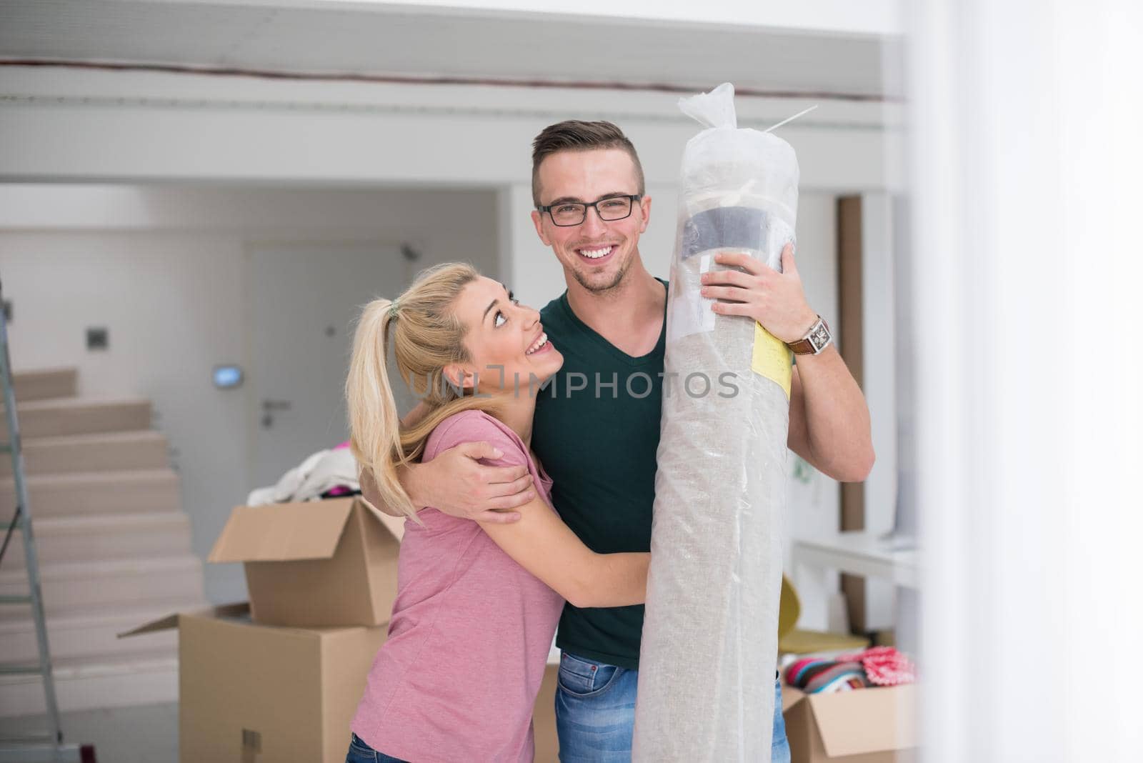 Young couple carrying a carpet moving in to new home together. Home, people, moving and real estate concept