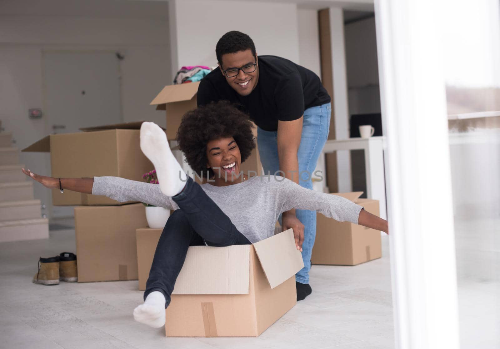 African American couple sitting in a box playing with packing material, having fun after moving in new home