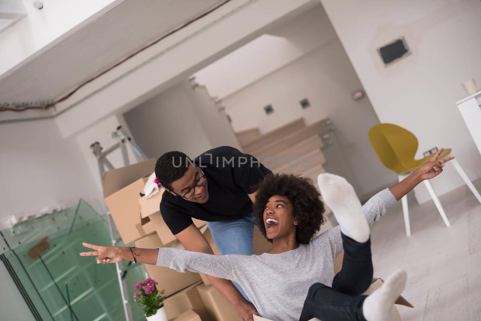 African American couple sitting in a box playing with packing material, having fun after moving in new home