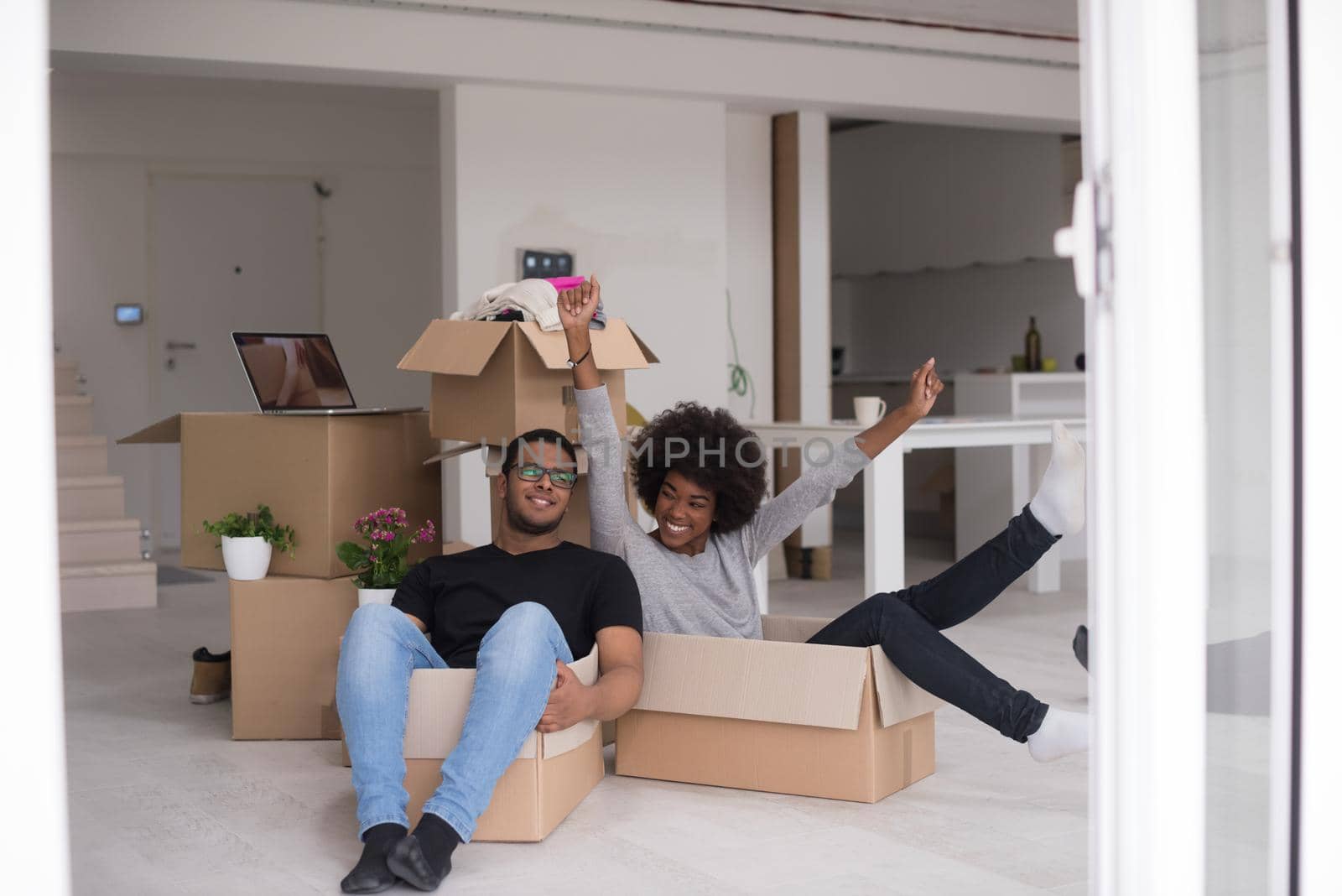 African American couple sitting in a box playing with packing material, having fun after moving in new home